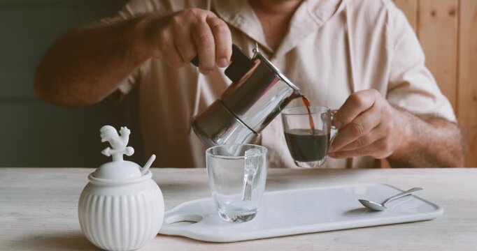 Man making coffee at home with traditional Italian neapolitan moka pot and pouring into a glass coffee cup. Preparation home coffee, morning ritual, coffee brewing process.