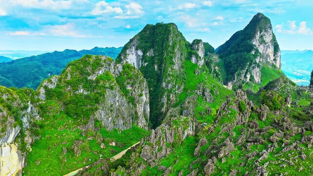 Lush karst mountain landscape in Guizhou, China, featuring towering limestone peaks, rugged ridges, forested valleys, and a winding road under a blue sky.