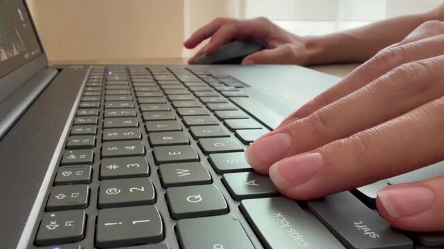 Female hands typing on a laptop keyboard and using a mouse at a desk. Remote work, office tasks, programming, or online communication in a modern workspace.