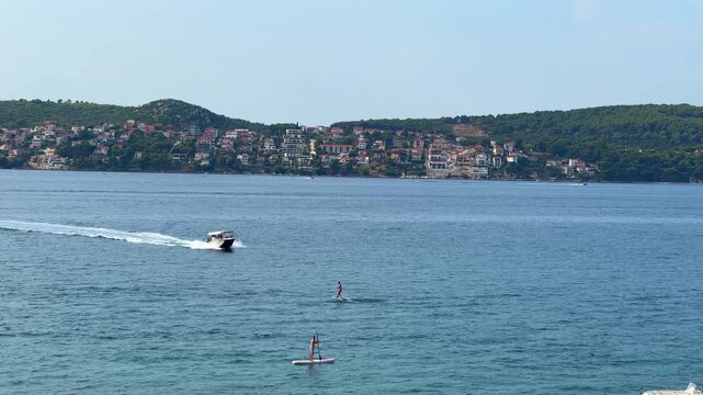 People paddleboarding on the sea with a coastal town and hills in the background