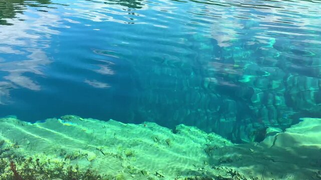 Crystal clear blue water of a natural spring with rocky bottom and gentle ripples