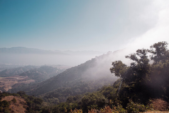 Scenic mountain landscape with thick clouds and mist rolling over green hills under bright blue sky