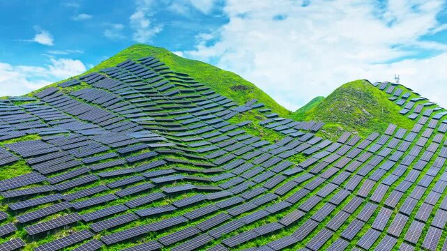 Renewable energy installation covers green mountain slopes with rows of photovoltaic panels beneath blue sky, illustrating clean electricity generation and sustainable infrastructure.