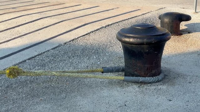 Mooring bollard with a thick rope on a concrete pier at the harbor