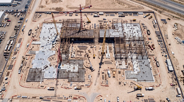 High angle aerial view of a large building construction site featuring heavy machinery, tall cranes, steel frameworks, and foundation work in progress.