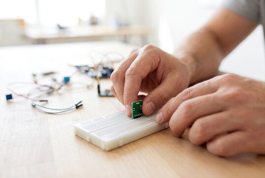 Hands placing a small green printed circuit board component onto a white breadboard