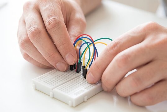 Hands carefully inserting colorful jumper wires into a white electronic breadboard