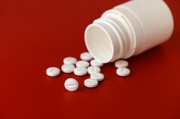In a close-up view, a white bottle tips over, releasing smooth, round tablets onto a bold red background. The bright colors highlight the simplicity and potential significance of the pills, inviting