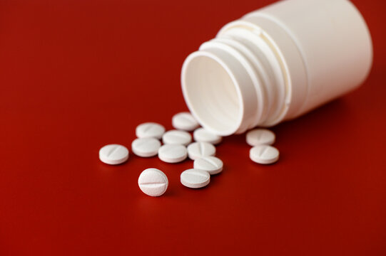 In a close-up view, a white bottle tips over, releasing smooth, round tablets onto a bold red background. The bright colors highlight the simplicity and potential significance of the pills, inviting