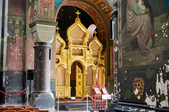 Interior of a historic Orthodox church. In the center &mdash; a carved gilded iconostasis with arched elements and crosses. Atmosphere of history, religion, and architectural heritage.