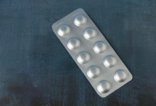 A blister pack containing ten round pills lies flat on a deep blue surface. The shiny metallic finish of the pills contrasts with the darker backdrop, creating an intriguing visual. This calm