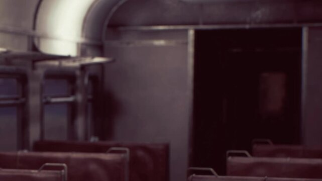 An old train interior shows empty seats lined up along the aisle. A dark corridor leads further into the train, giving a glimpse of the vintage style. The setting has a quiet feel.