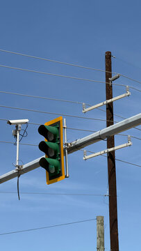 Traffic signal and surveillance camera at an urban intersection with power lines and blue sky