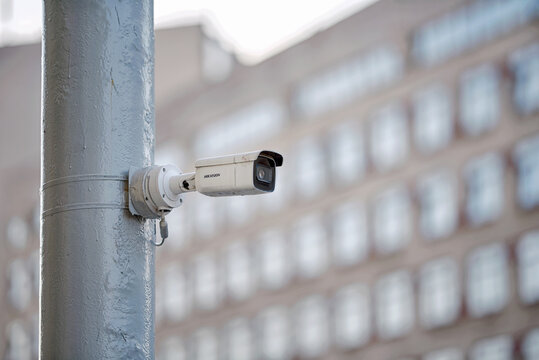 Minsk, Belarus. Apr 4, 2025. White Hikvision security camera mounted on gray metal pole outdoors with blurred multi story building, rows of windows in soft background. Hikvision - Chinese manufacturer