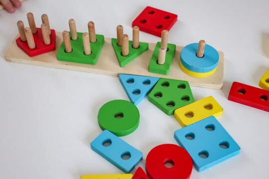 Colorful Montessori wooden shape sorting toy with geometric blocks on a white table.