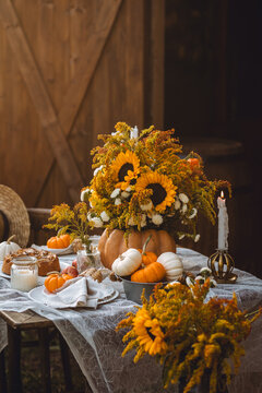 Centrepiece floral composition with natural sunflowers in a pumpkin vase. Beautiful fall seasonal wedding decor or thanksgiving family dinner arrangement outdoors. Countryside style, cottage core
