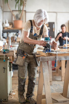 Carpenter works with handheld electric router machine on rail track with additional stabilization handle, professional craftsman using special instrument to process surface of antique wooden door.