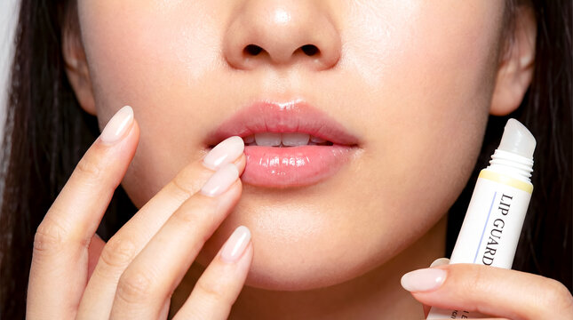 Woman applies lip balm to lips for moisture. Clean background highlights focus on lips and hands. Concept of beauty products, skincare, cosmetics