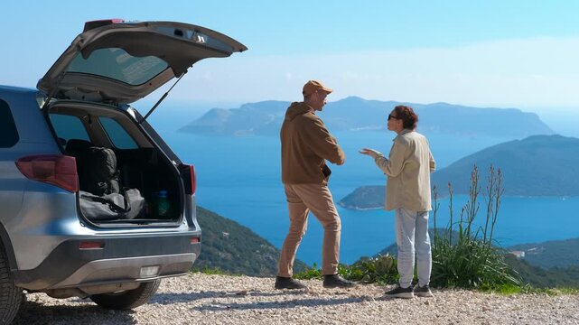 Quarrel on a journey. Young couple having a disagreement and arguing near their car during a scenic road trip, eventually standing back-to-back with arms crossed against a beautiful mountain backdrop