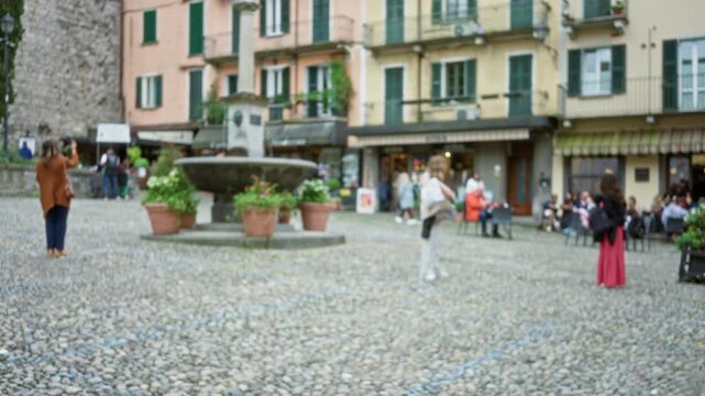 Blurred cobblestone scene with fountain and storefronts, soft bokeh plaza; background backplate copyspace calm.