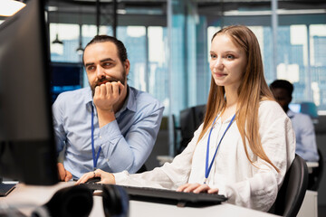 Obraz premium Senior team leader mentors a junior developer at an office desk and teaches coding best practices, guiding the female intern through technology company project tasks during workplace training.