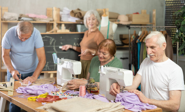 In sewing workshop coterie school, elderly people learn craft of tailor. Participants chatting, cut fabric and paper, sewing. Interest group, activities for elderly, hobbies.