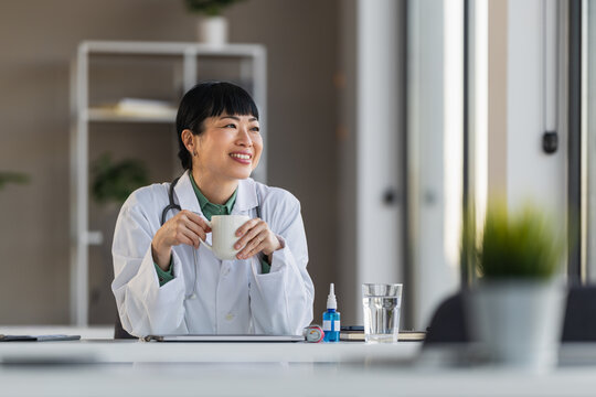 Female doctor enjoying coffee break in medical office while smiling and looking out window