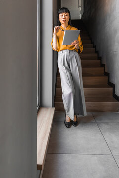 Businesswoman reading tablet while leaning in modern office stairwell with thoughtful expression