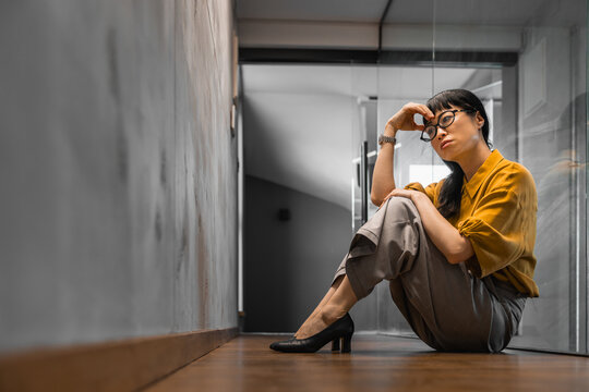 Young professional woman sitting on office floor looking stressed and thoughtful in hallway