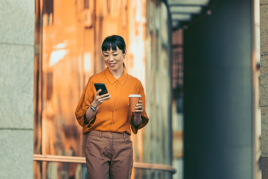 Woman walking in city with smartphone and coffee during morning commute