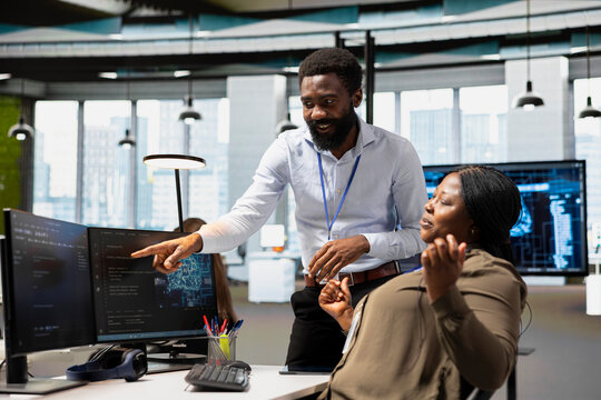 Manager oversees AI project development in an office, guiding an employee through machine learning tasks and mentoring the developer on neural network implementation during a technology project.