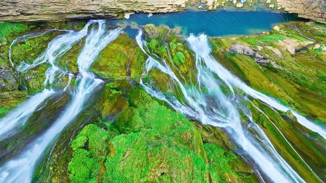Turquoise pool feeds a cascading waterfall over moss-covered limestone, creating a vivid natural landscape for travel, tourism, and environmental imagery.