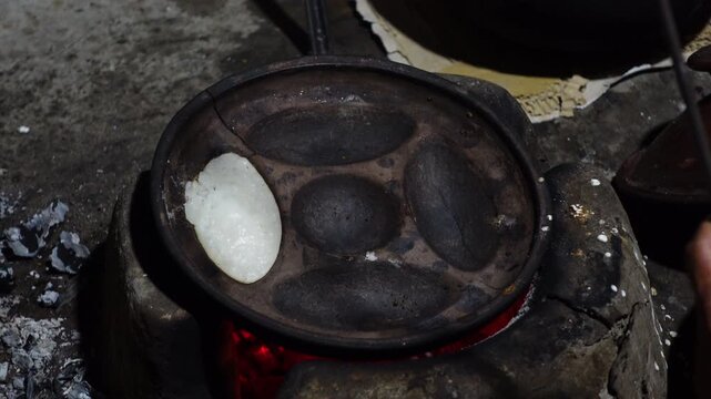 A woman brings out the finished Chitai Pitha in a hot clay oven. Chitai pitha is being made in a terracotta mold for making pitha in a heated clay oven.