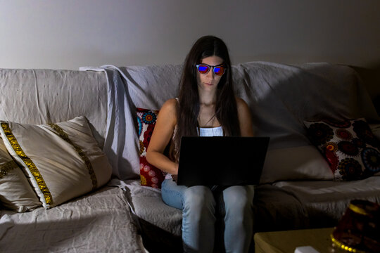 Woman wearing blue light blocking glasses working on laptop at home at night