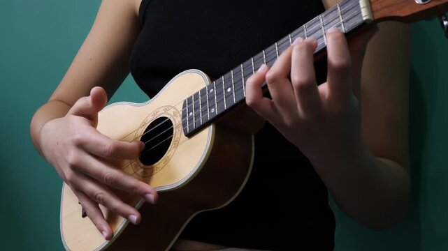 Woman playing acoustic ukulele in close-up against teal studio backdrop