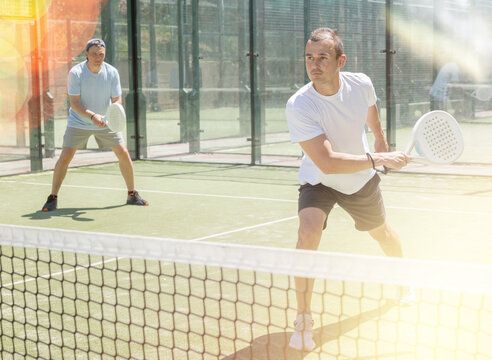 Young man and adult man in doubles playing paddle tennis on tennis court