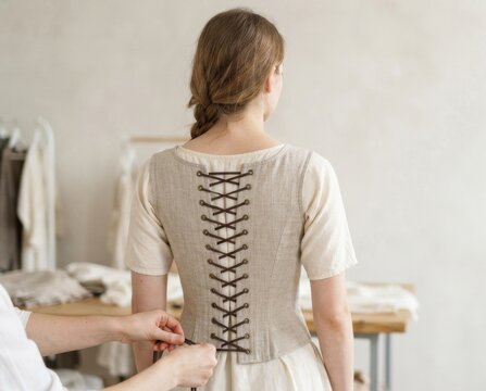 Back view of a woman having a linen corset laced. Historical costume fitting and dressing process