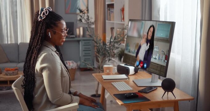 Cheerful young Black woman chats with a friend holding her baby during a warm video call on a computer at home.