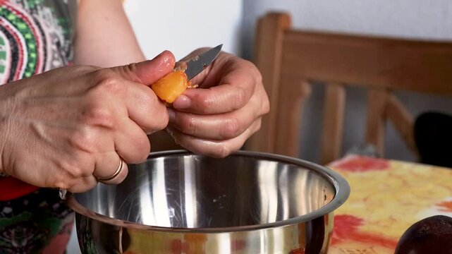 Woman slicing very ripe juicy peach with a small knife over a metal mixing bowl. Home cooking 

