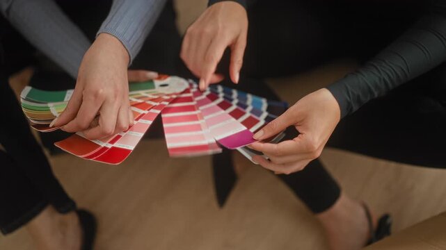 Woman holding a fan of color swatches, hands flipping paint chips in studio; creative collaboration focused.