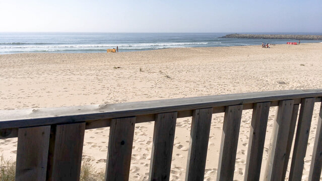 Point of view shot of a wooden railing overlooking a sandy beach and ocean waves in Paramos Portugal