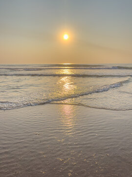 Golden sunset casting a brilliant reflection over gentle ocean waves washing onto a smooth wet sandy beach