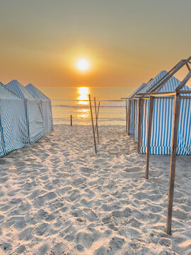 Striped beach tents on sandy shore during golden sunset