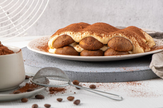 Homemade traditional Italian tiramisu dessert served on a white plate with cocoa powder and coffee beans