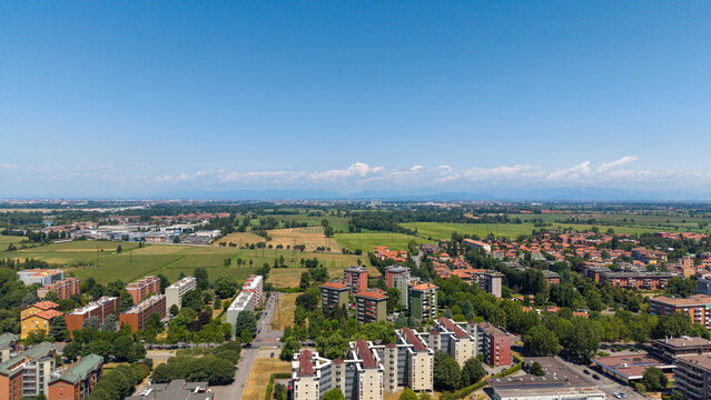 Panoramic View of Italian Town: An expansive aerial perspective captures a sprawling Italian town nestled amidst verdant fields and distant, hazy mountains under a clear blue sky.