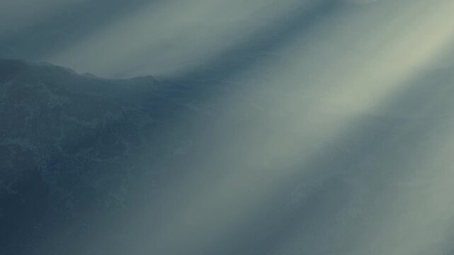 Light beams break through clouds and shine on mountain terrain. The atmosphere looks foggy and dark, creating an interesting visual effect. The time of day is unclear.
