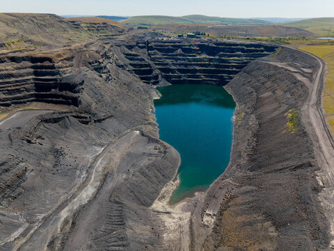 Aerial view over massive disused surface coal mine, steep terraced walls surrounding deep flooded pit, former industrial extraction site undergoing natural filling