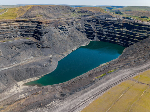 Flooded pit crater at Ffos-y-Fran opencast coal mine, Merthyr Tydfil, abandoned industrial mining site with exposed dark rock terraces in South Wales.