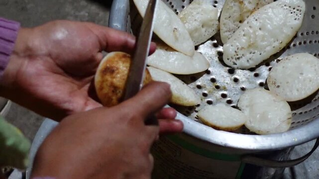 The burnt parts of the hot chitai pitha, made by mixing rice flour with water and salt, are cleaned with a knife. 