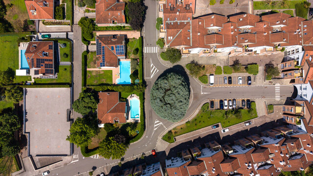 An overhead perspective reveals a tranquil residential area, featuring a roundabout surrounded by charming houses with red-tiled roofs, swimming pools. Bellaria, Peschiera Borromeo, Italy